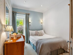 A bedroom with a bed, bedside table, lamp, and curtains.