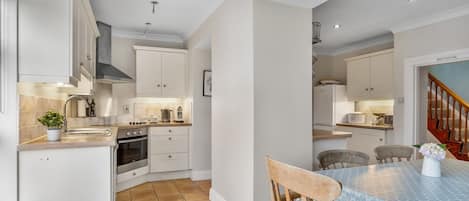 A kitchen with white cabinets, a dining table with chairs, and a staircase leading to another level.