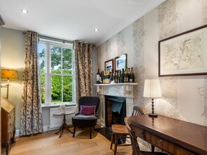 A room with a fireplace, a dining table, a chair, a window with curtains, and a wall-mounted shelf with bottles. - Hill House Clifden (Clifden)