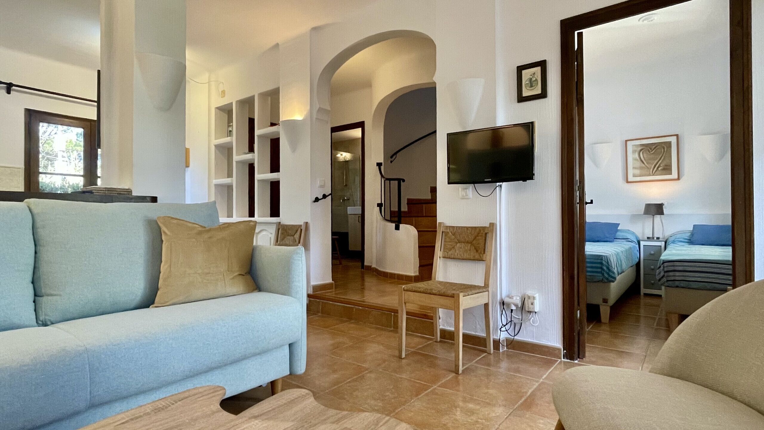 Un salon avec un canapé, un téléviseur et un escalier, ainsi qu’une chambre à coucher avec deux lits.