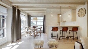 Una cucina moderna con mobili in legno, un'area pranzo con un tavolo e sedie rotonde, e un soggiorno con un divano e pouf.