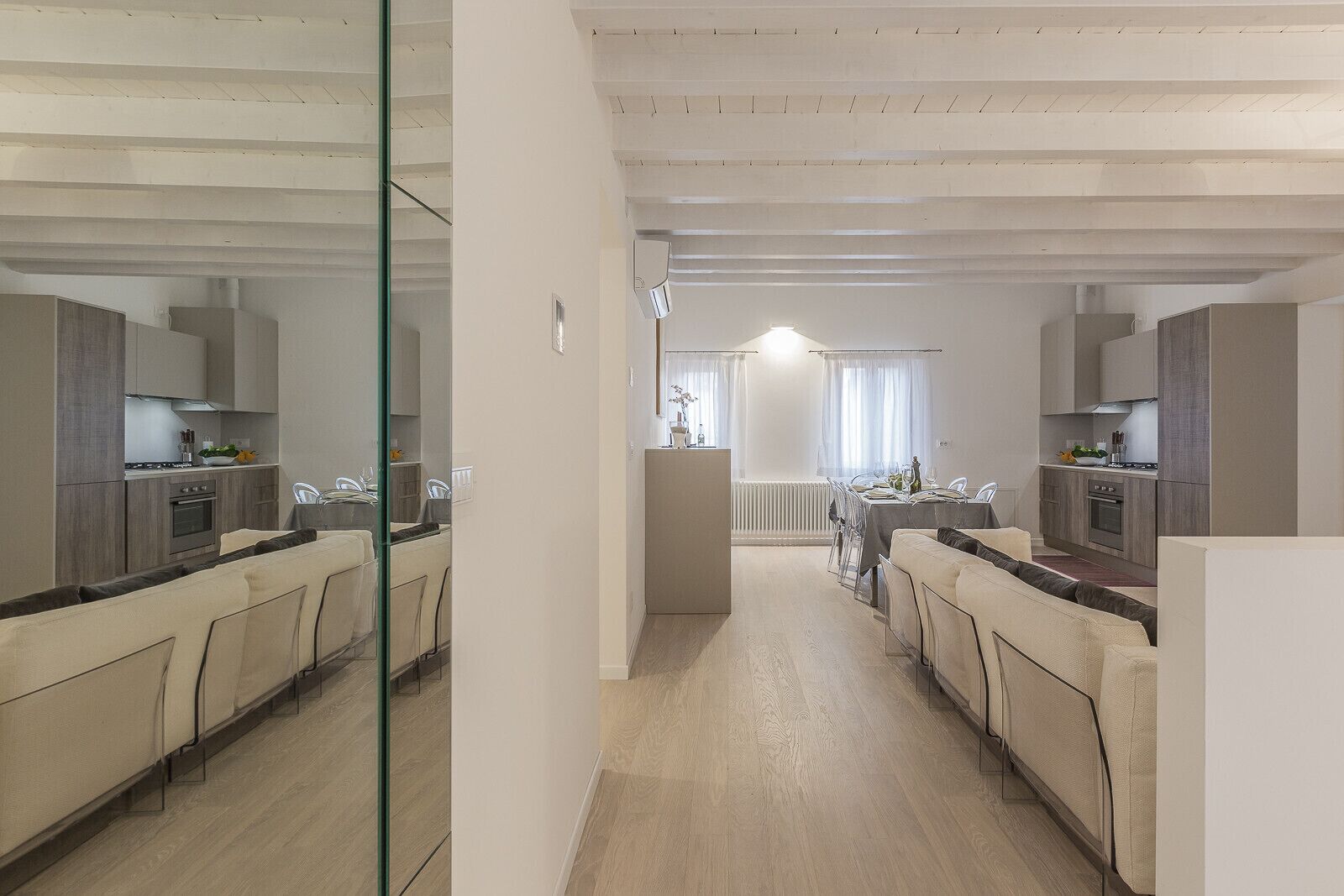 Une cuisine moderne dotée d’un îlot central, d’un coin repas avec une table et des chaises, et d’un mur miroir qui agrandit visuellement l’espace.