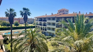 A multi-story hotel with balconies, a swimming pool, and palm trees.