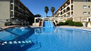 Una piscina con un tobogán azul, rodeada de edificios con balcones y palmeras.