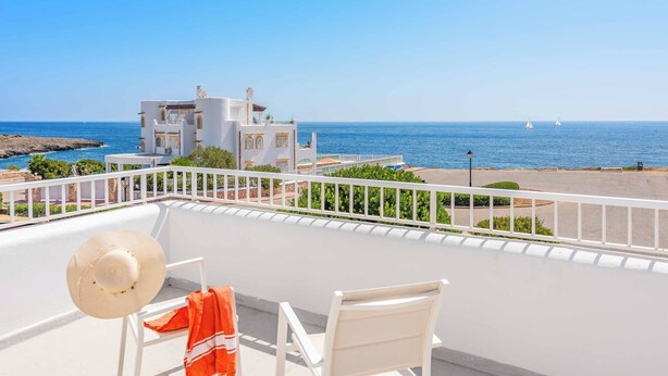 A balcony with white chairs, a straw hat, and a red towel. A white building with a balcony is visible in the background. - Villa Fort View - Four Bedroom Villa, Sleeps 8 (Santanyí)