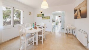A bright kitchen with white cabinetry, a dining table with chairs, a hanging light fixture, and a view of the outside through a window. - Villa Fort View - Four Bedroom Villa, Sleeps 8 (Santanyí)