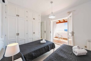 A hotel room with two beds, a ceiling fan, and a view of the sea through an open door.