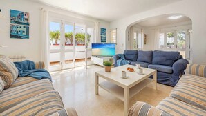 A living room with a sofa, a coffee table, and a TV. There are potted plants and a view of the outside. - Villa Fort View - Four Bedroom Villa, Sleeps 8 (Santanyí)