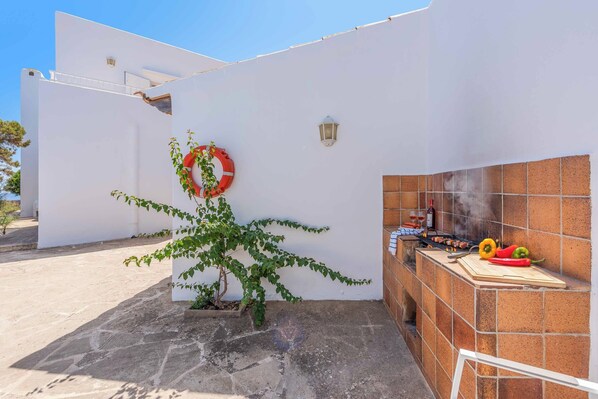 A patio area with a barbecue grill, a small plant, and a white wall with a life ring.