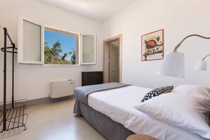 Ein Schlafzimmer mit Bett, Heizkörper, Fenster, Tür und einer Wandlampe.