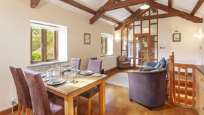 A dining area with a wooden table and chairs, a sofa, and a staircase with wooden railings. - The Granary, Luxborough (Luxborough)