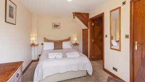 A bedroom with a bed, bedside lamps, a wooden headboard, a dresser, a chair, and a mirror. - The Granary, Luxborough (Luxborough)