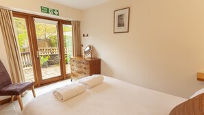 A hotel room with a bed, a dresser, a chair, a fire exit sign, and a view through the glass door. - The Granary, Luxborough (Luxborough)