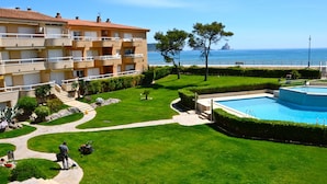 Área externa bem cuidada com piscina, vista clara para o mar e um edifício com varandas.