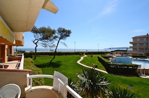 A balcony with a view of a landscaped garden, a swimming pool, and a building with balconies.