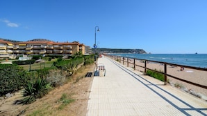 Um calçadão à beira-mar com um passeio pavimentado, bancos e uma praia.