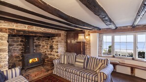 A cozy room with a stone fireplace, a striped sofa, and a view of the sea through large windows. - The Crows Nest, Porlock Weir (Somerset)