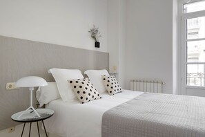 A neatly made bed with white bedding and polka dot pillows, a small round table with a white lamp, and a radiator on the wall. - Zubieta Suite by FeelFree Rentals (San Sebastián)