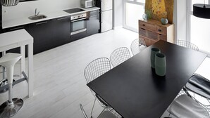 Una cocina moderna con una paleta de colores blanco y negro, electrodomésticos de acero inoxidable y un comedor con una mesa negra y sillas de alambre.