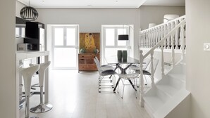 Una cocina moderna con electrodomésticos de acero inoxidable, una zona de comedor con sillas blancas y una escalera con barandillas blancas.