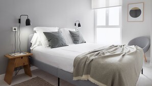 Un dormitorio minimalista con cama, lámparas de noche, una mesita de madera y una silla.