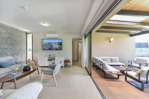 Un salon moderne doté d’un téléviseur à écran plat, d’un canapé, d’une table à manger et d’un espace balcon avec des sièges d’extérieur.