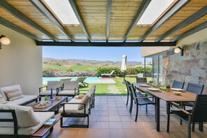 Une terrasse couverte, aménagée avec du mobilier d’extérieur, une piscine et une vue sur le paysage.
