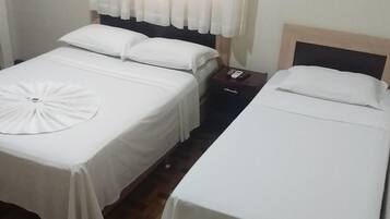 A hotel room with two beds, each with white bedding and a circular decorative item on the bed. There is a nightstand with a phone and a small drawer.