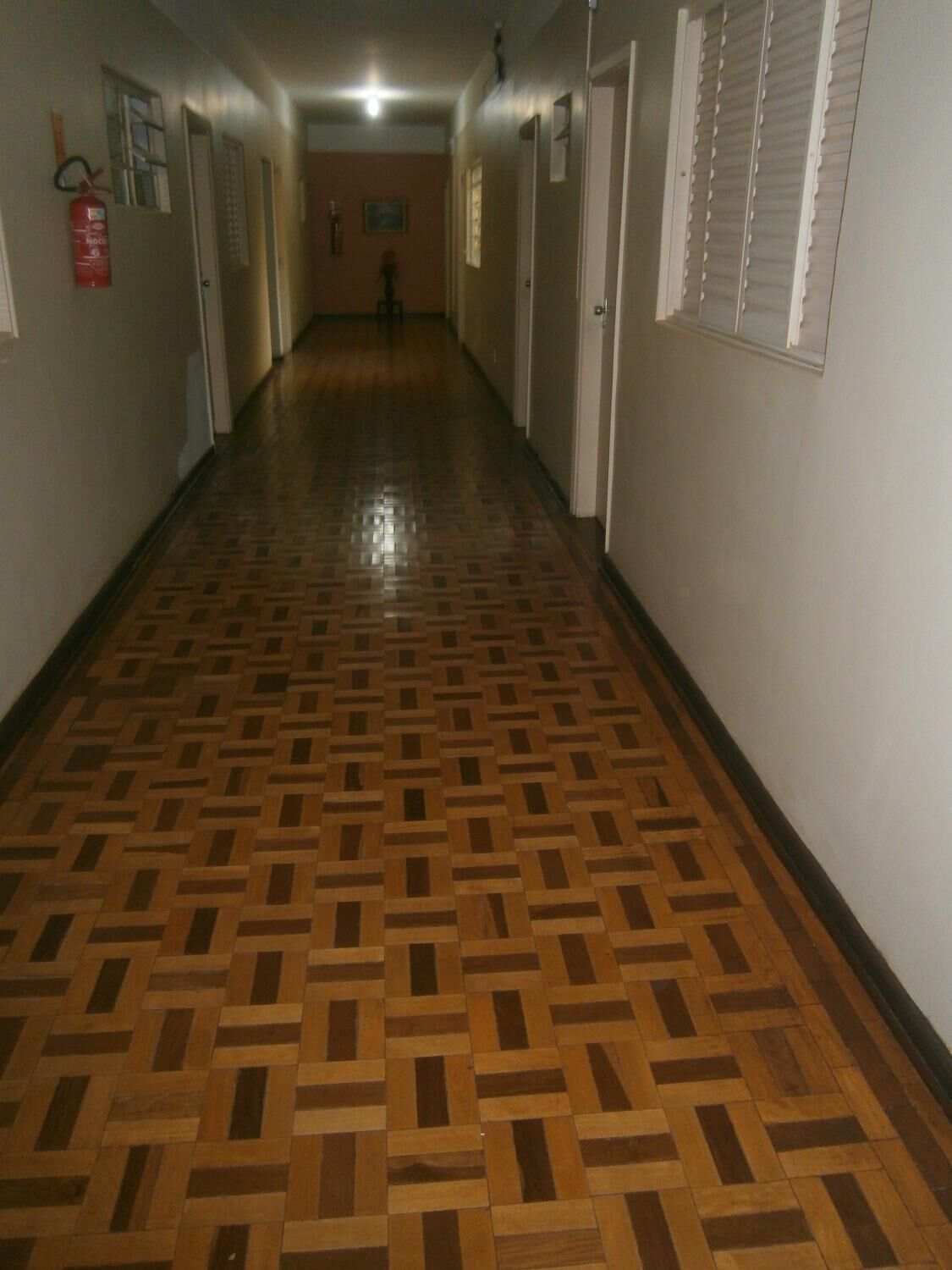 Un pasillo con suelo de madera estampado, puertas a ambos lados y un extintor en la pared izquierda.