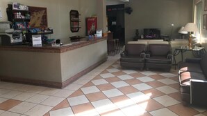 Een hotel lobby met een receptiebalie, een zithoek met banken, een televisie en een Coca-Cola koelkast.