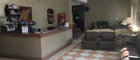 A hotel lobby with a reception desk, a seating area with sofas, a television, and a Coca-Cola refrigerator.