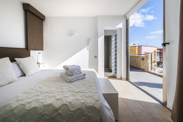Une chambre à coucher avec un lit, des oreillers, une serviette pliée et une vue sur l’extérieur, accessible par une porte coulissante.