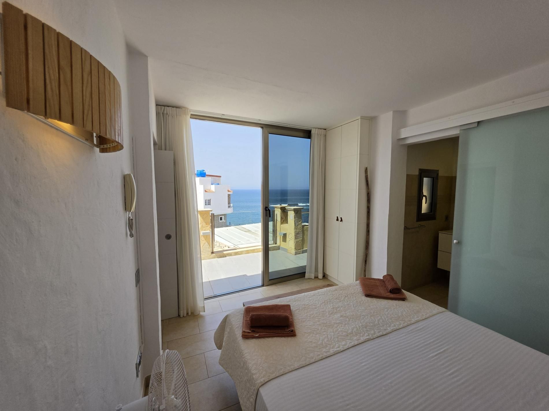 A hotel room with a bed, a view of the sea, and a sliding glass door leading to a balcony.