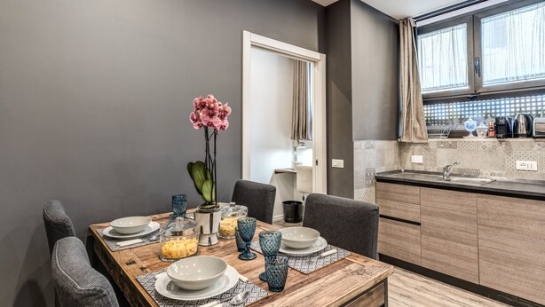 A modern kitchen with a wooden dining table set for four, a sink, and a window with curtains.
