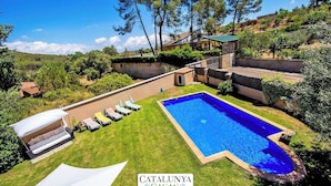 A pool area with a white canopy and lounge chairs, surrounded by lush greenery and a hillside backdrop.
