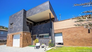 A modern two-story house with a flat roof, a garage, and a small patio area with outdoor furniture.