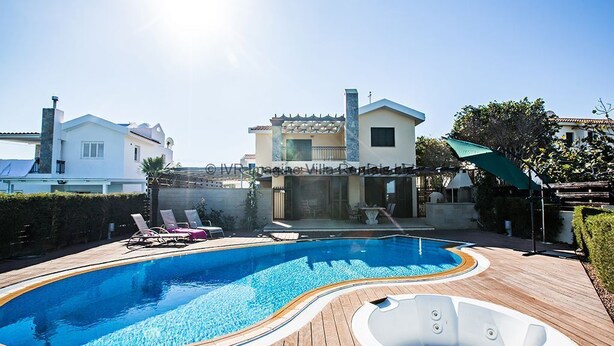 Una piscina con un solarium in legno, sedie a sdraio e una vasca idromassaggio.