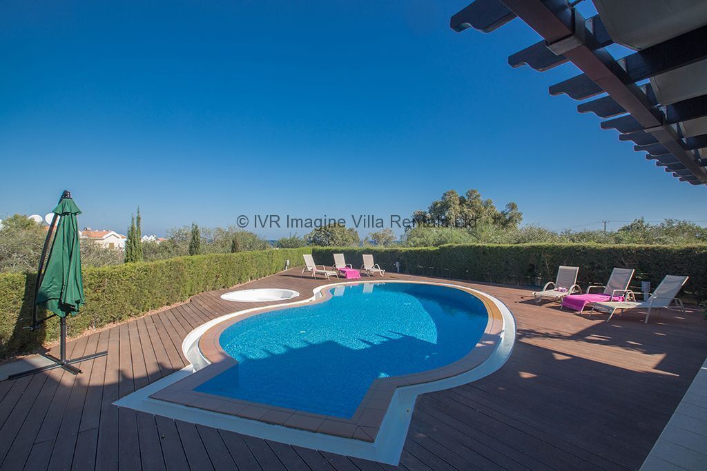 A swimming pool with a wooden deck, lounge chairs, and a green umbrella.