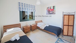 Una camera da letto con due letti, una finestra con tenda a quadri blu, un quadro appeso al muro raffigurante un'auto e una porta di legno con pannello decorativo.