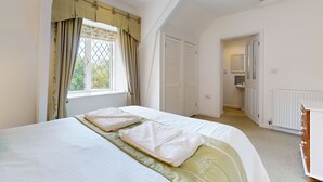 A bedroom with a bed, a window with curtains, a door leading to a bathroom, and a radiator. - Plum Tree Cottage, Porlock (Porlock)