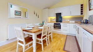 A modern kitchen with white cabinets, a wooden dining table, and a built-in oven. - Plum Tree Cottage, Porlock (Porlock)
