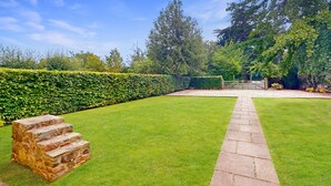 A well-maintained garden with a stone pathway leading to a wooden gate, surrounded by hedges and trees. - Plum Tree Cottage, Porlock (Porlock)