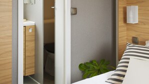 A modern hotel room with a wooden wardrobe, a bedside table, a bed with striped pillows, and a green plant. - OCEANBAHIA12 rental luxury 6 pers Club 5 * clim Montalivet Aquitaine  (Vendays-Montalivet)