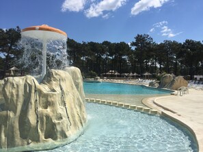 A swimming pool with a water feature, surrounded by lounge chairs and umbrellas. - OCEANBAHIA12 rental luxury 6 pers Club 5 * clim Montalivet Aquitaine  (Vendays-Montalivet)