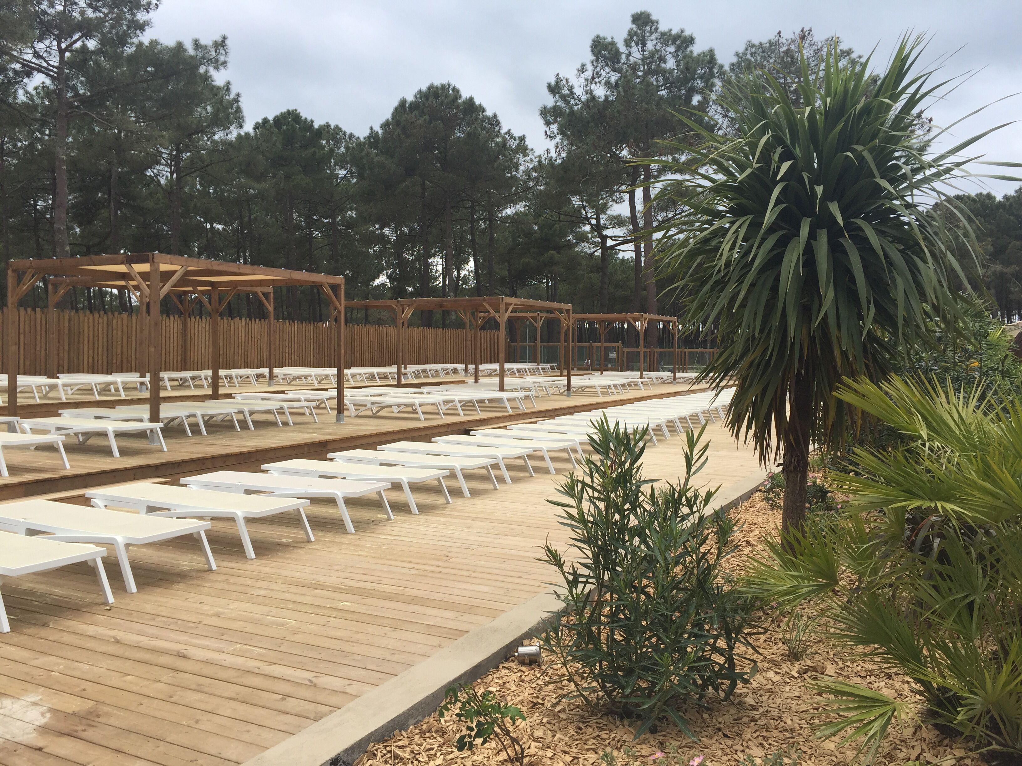 Una terraza de madera con sillones blancos y una estructura de pérgola de madera.
