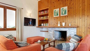 Uma sala de estar aconchegante com sofás laranja, uma estante de madeira, uma lareira e uma televisão.