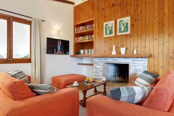 A cozy living room with orange sofas, a wooden bookshelf, a fireplace, and a television.