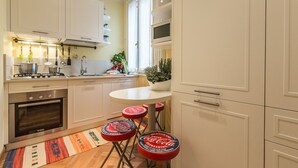 A compact kitchen with white cabinets, a Bosch oven, a gas stove, and a small island with stools. - Ca' Dei Nomboli Canal View (Venice)