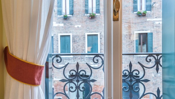 A window with a curtain and a balcony railing. - Ca' Dei Nomboli Canal View (Venice)