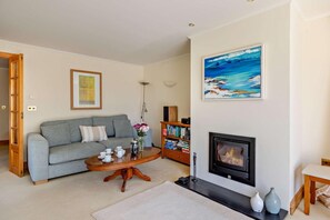 Una sala de estar con sofá, mesa de centro, chimenea, estantería y un cuadro en la pared.